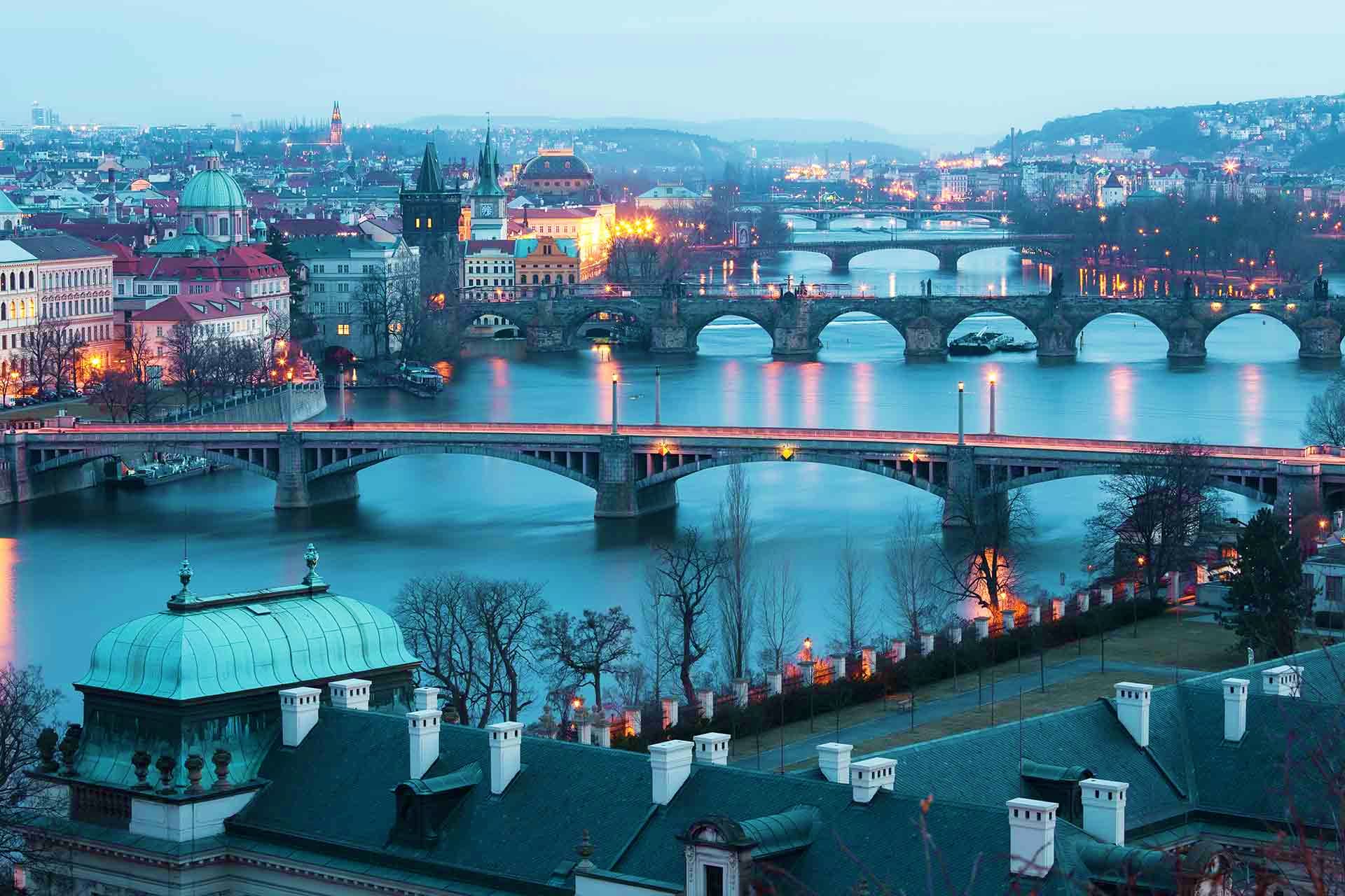 Prague cityscape at dusk showing Vltava River with multiple historic bridges and illuminated architecture